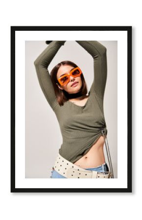 A young woman with brunette hair striking a pose in a green shirt and orange sunglasses.