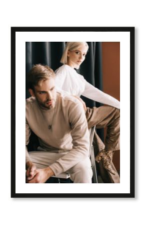 blonde woman in white blouse and bearded man sitting on chair near curtain
