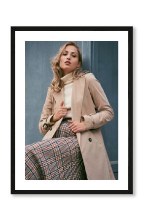 Beautiful casual blond girl in trench coat confidently looking in camera outdoor