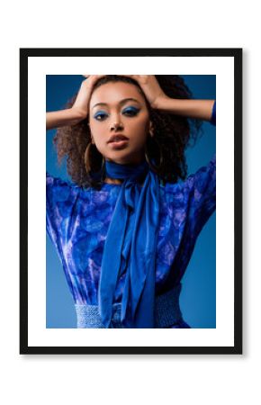 attractive african american woman in stylish dress looking at camera isolated on blue