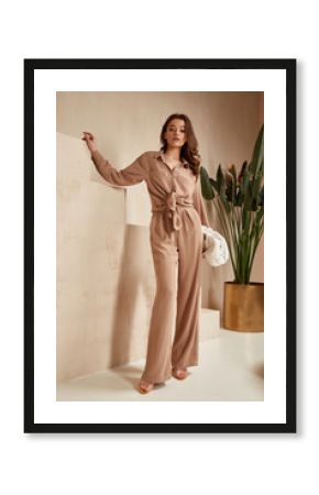 Beautiful brunette woman natural makeup wear fashion clothes casual dress code office style total beige blouse and pants suit, romantic date business meeting accessory bag interior stairs flowerpot.