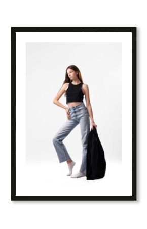 Model posing in casual outfit with black top and denim jeans in a minimalist studio setting during a fashion photoshoot