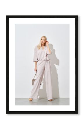Stylish woman posing against a white wall in a wide beige blouse and trousers
