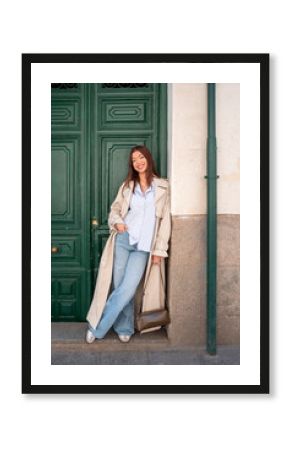 Young tourist woman leaning against a green door is smiling at camera