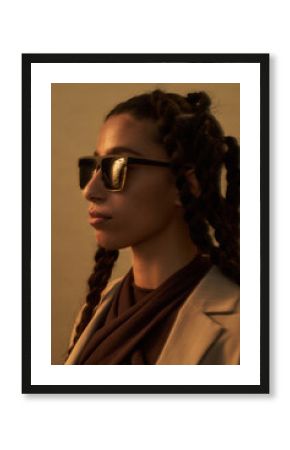 Young adult Middle Eastern woman wearing sunglasses standing in profile with braided hair, looking away from camera, neutral expression, soft lighting highlighting facial features