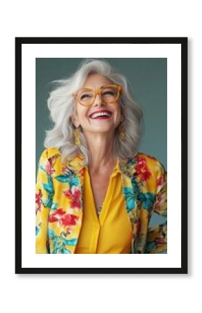 Vibrant portrait showcasing modern senior fashion with bright yellow floral blazer, stylish orange glasses, and silver wavy hair against teal background, expressing joy and confidence.