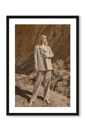 stylish female model standing on beach near rocky cliff
