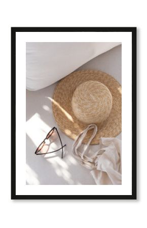 Flatlay of women's fashion accessories. Stylish female sunglasses, straw hat, shopper bag on white lounge couch with pillows. Top view