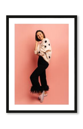 Full length pretty young caucasian girl posing for camera with smile on her face in studio. Brunette with bob haircut wears warm sweater and pants. Good mood, fashion trends