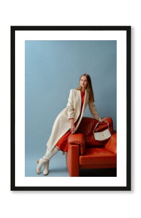 Fashionable confident woman wearing elegant white woolen coat,  high leather heeled boots, with stylish bag, posing on blue background. Full-length studio fashion portrait. 
