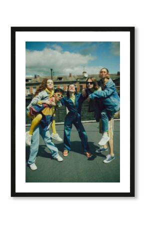 Joyful urban fashion vibe. Lively group of five friends enjoy sunny day on rooftop, wearing stylish denim clothes. Carefree, youthful spirit. Concept of 90s, fashion, youth culture, old-style trends
