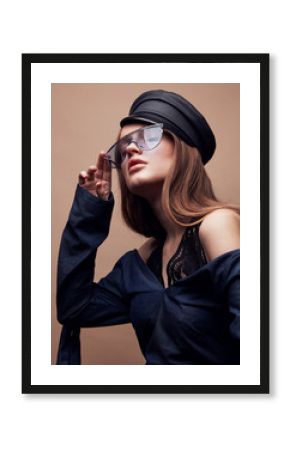 Fashion portrait of beautiful young woman in black leather beret cap, denim blouse and blue retro sunglasses