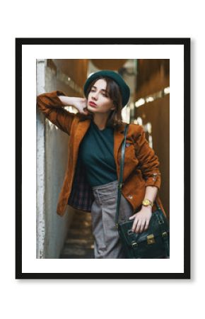 Outdoor fashion portrait of young woman wearing trendy corduroy blazer, green beret, checkered trousers, golden wrist watch, carrying leather bag,  posing in street of European city