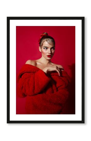 Beautiful attractive girl with smooth hair and in a red fur coat made of faux fur posing in the studio on a red background.