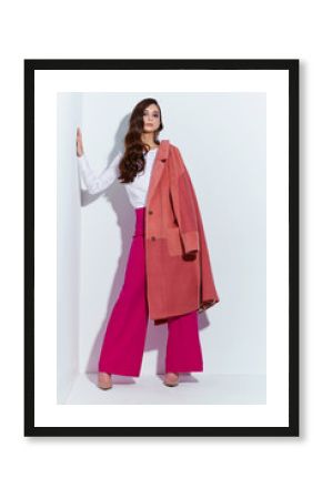 High fashion portrait of young elegant woman. Coral coat, magenta pants, white blouse.