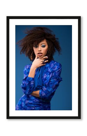stylish african american woman with makeup in dress looking at camera isolated on blue