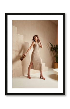 Sexy beautiful woman brunette tanned skin makeup cosmetic fashion clothes summer collection beige cotton dress accessory bag style summer journey walk date beach wear interior stairs leaves flowerpot.