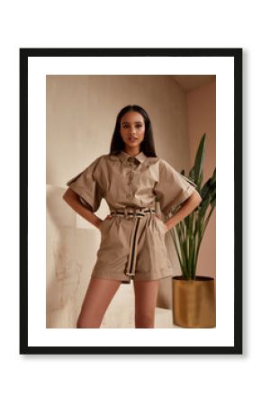 Beautiful woman fashion model brunette hair tanned skin wear beige overalls button suit sandals high heels accessory clothes style journey safari summer collection plant flowerpot wall stairs.