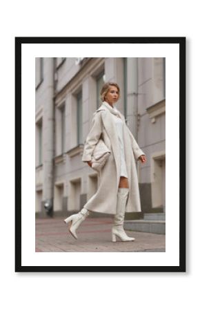 Elegant woman in white dress, hessian boots and coat waling at city street. Fall autumn fashion look. Pretty tall stylish young gitl with fashionable makeup and hair style. Elegant lady. Full length