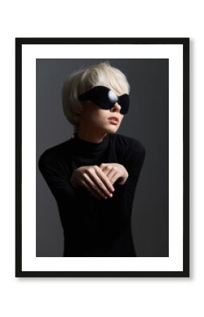 Stylish woman in black turtleneck and oversized sunglasses, posing delicately with hands, evoking a sense of high fashion and modern elegance against a dark backdrop.