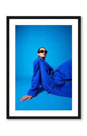 Woman in blue suit and sunglasses fashion portrait studio shot against blue backdrop