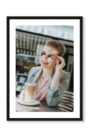 Mid adult woman wearing sunglasses with coffee glass sitting in sidewalk cafe on sunny day