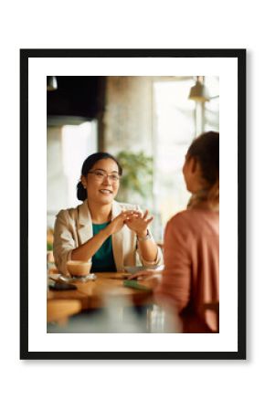 Happy Asian entrepreneur talks to her colleague during coffee break in cafe.