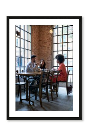 Side view of group of friends or co-workers talking in modern cafe in morning.