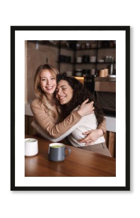 Happy girls friends sitting in cafe talking with each other drinking tea or coffee.