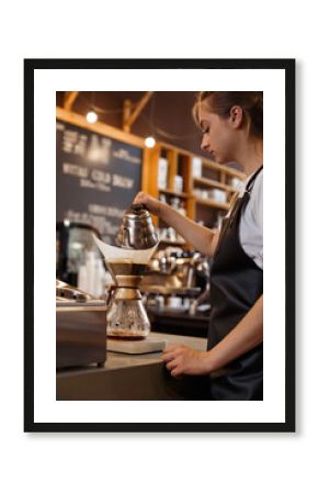 Professional barista preparing coffee using chemex pour over coffee maker and drip kettle. Young woman making coffee. Alternative ways of brewing coffee. Coffee shop concept.
