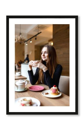 Young woman drinks tea in a cafe and enjoys a delicious dessert