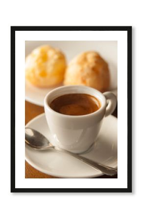 cup of espresso coffee viewed from the front with cheese breads in the background