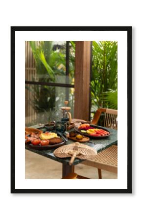 Breakfast in upscale luxury tropical cafe with pineapple, dragonfruit, watermelon, and papaya, served on a banana leaf on a wood plate with lime and American breakfast with egg, hashbrown, and sausage