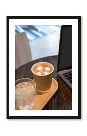 Close-up of Hot coffee latte with latte art milk foam in cup made of paper and laptop computer on wood desk office desk in coffee shop at the cafe,during business work concept