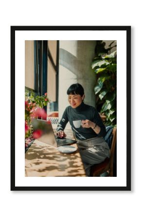 Asian freelancer woman working remotely from coffee shop using laptop and drinking coffee