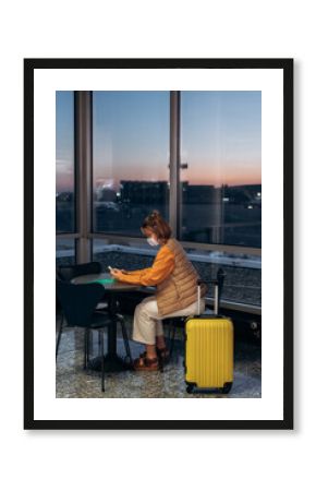 Female traveler using smartphone in airport cafe