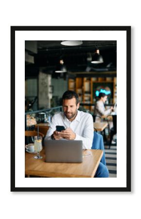 Male entrepreneur text messaging on smart phone while working in cafe.