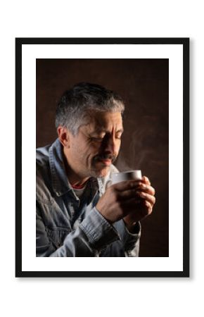 portrait d'un homme qui boit un café ou un thé. Il tient une tasse fumante dans ses mains pour se réchauffer