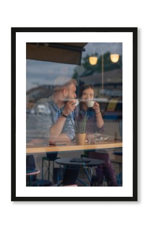 two friends sitting together in a cafe, drinking coffee. shot thought window with reflections.