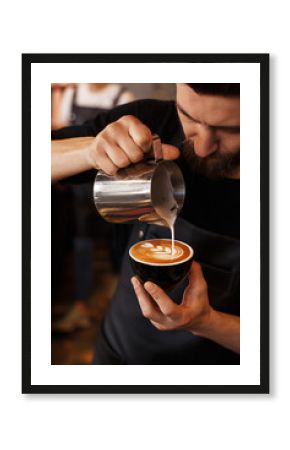 Young smiling male barista making cappuccino. Pouring milk for prepare cup of coffee. Latte art. Morning cup of coffee in café. Brewing coffee. Coffee shop concept.