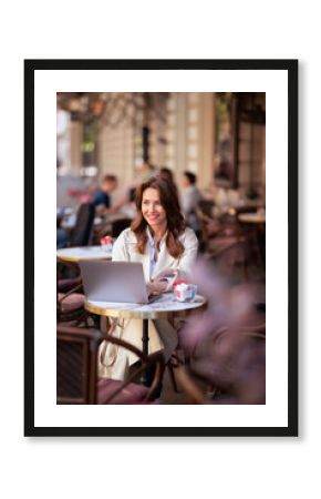 Businesswoman working on laptop and smiling at outdoor cafe