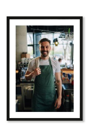 Smiling barista wearing apron and holding cloth in cafe
