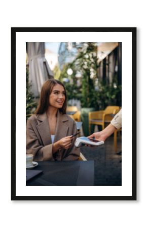 Positive, cheerful facial expression. Woman is paying for food in cafe by using credit card. Conception of wireless money transfer