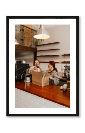 A female employee stands behind the bar and holds a cup next to which the female owner, who stands next to her, holds her hands, before the cafe opens