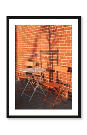 chairs and table of street cafe against brick wall at sunset