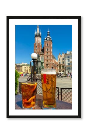 A dark and wheat beer standing on a small table on the square in Cracow, Poland, with the view on St. Mary's Basilica. The two bell towers od the basilica are towering above the city. Sunny day