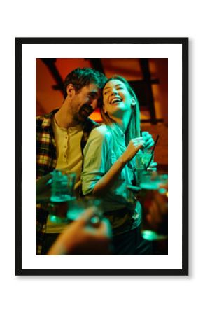 Young happy couple laughing while drinking and having fun in a pub at night.