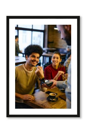 Happy man using smart watch while making contactless payment to waiter in a pub.