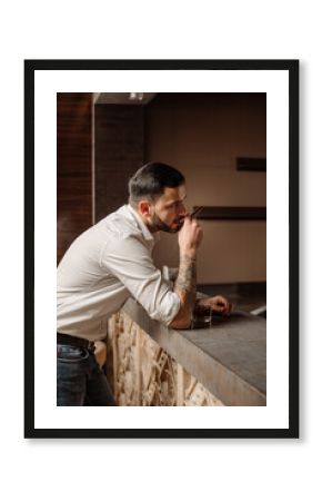 Handsome bearded male in shirt and jeans with glass of whiskey and cigar in the bar or pub