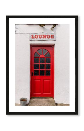 Sign for the lounge above the red door at the entrance to an Irish pub.